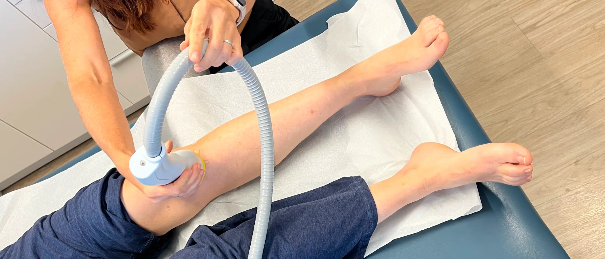 Clinician applying a shock wave therapy handpiece to a patient's lower leg on an exam table